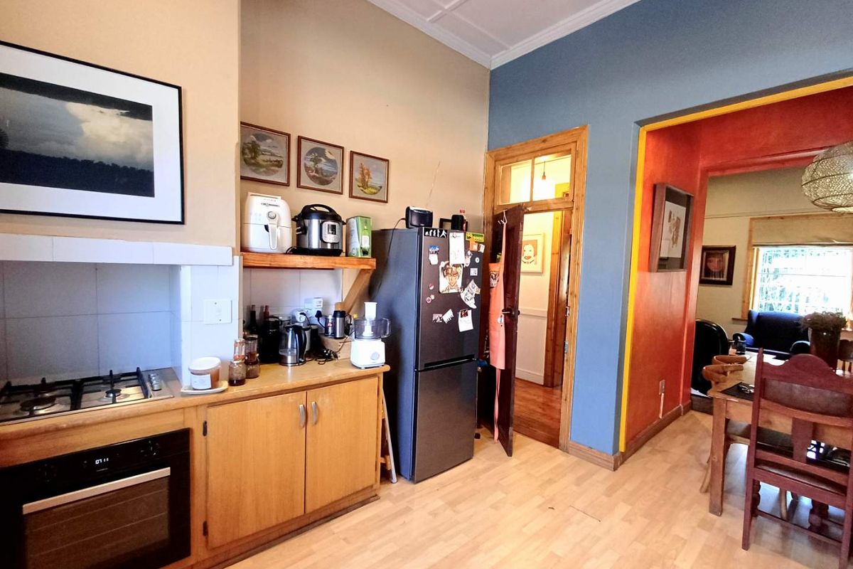 A functional kitchen featuring built-in oven, gas hob, and wooden cabinetry, with an open-plan layout leading into the adjacent dining area.