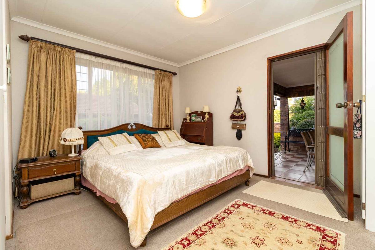 A well-lit bedroom featuring neutral walls, carpeted flooring, and direct access to an outdoor patio area through a wooden door.