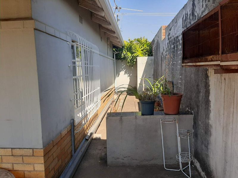 A narrow side passage featuring a brick boundary wall, security bars on the window, and concrete paving.