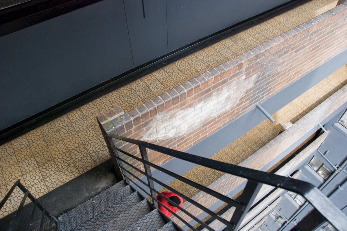 An elevated view of an exterior metal staircase and brick retaining wall showing signs of weathering and efflorescence.