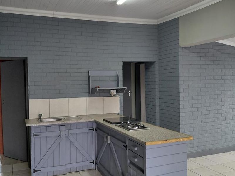 A compact kitchen featuring grey painted brick walls, custom timber cabinetry, a gas hob, and tiled flooring in an open-plan layout.
