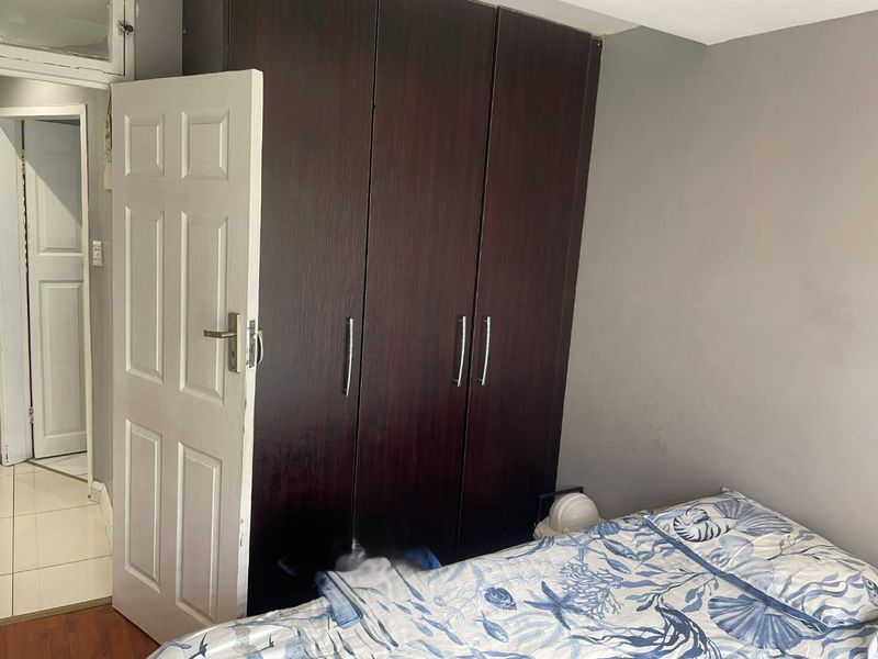 A bedroom featuring dark wood built-in wardrobes, laminate flooring, and a classic panel door leading to an adjacent hallway.
