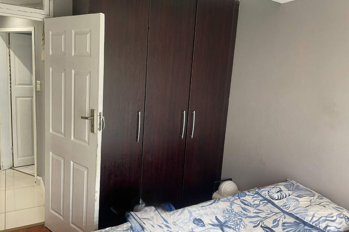 A bedroom featuring dark wood built-in wardrobes, laminate flooring, and a classic panel door leading to an adjacent hallway.