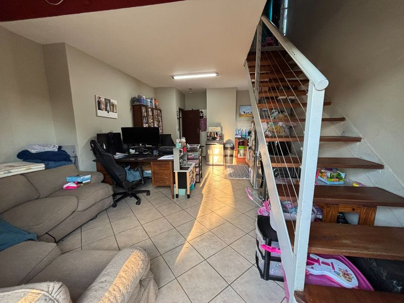 Open plan living area featuring tiled flooring and a central staircase, leading towards a compact kitchen space with built-in cabinetry.