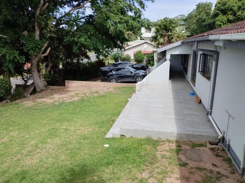 A rear view of the property featuring a tiled patio area, lawn, and established trees, providing a functional outdoor space.