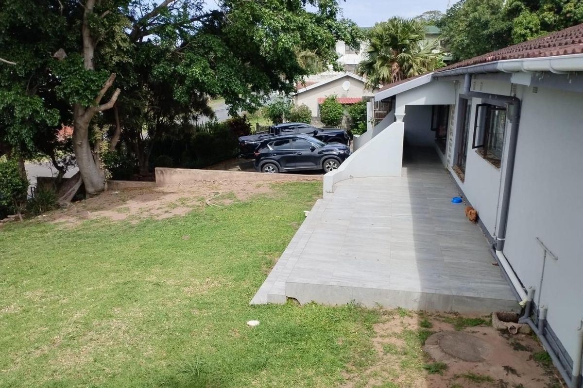 A rear view of the property featuring a tiled patio area, lawn, and established trees, providing a functional outdoor space.