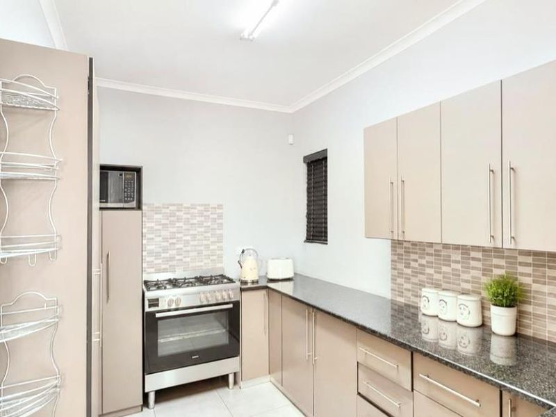 A functional kitchen featuring granite countertops, a gas stove with oven, built-in microwave, and ample cabinetry with a modern tiled backsplash.