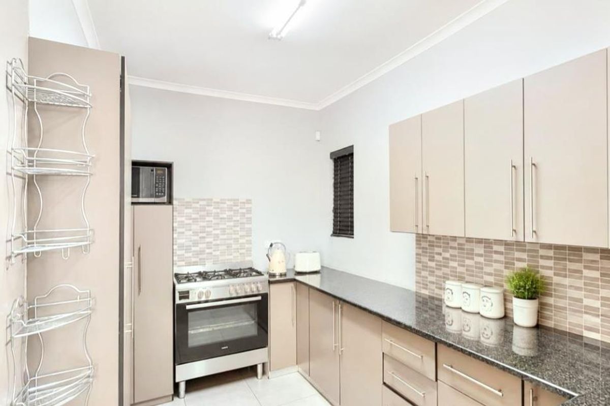 A functional kitchen featuring granite countertops, a gas stove with oven, built-in microwave, and ample cabinetry with a modern tiled backsplash.