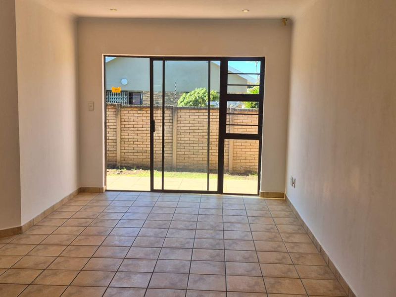 An empty living room featuring tiled flooring and a large sliding glass door providing access to the rear outdoor area.