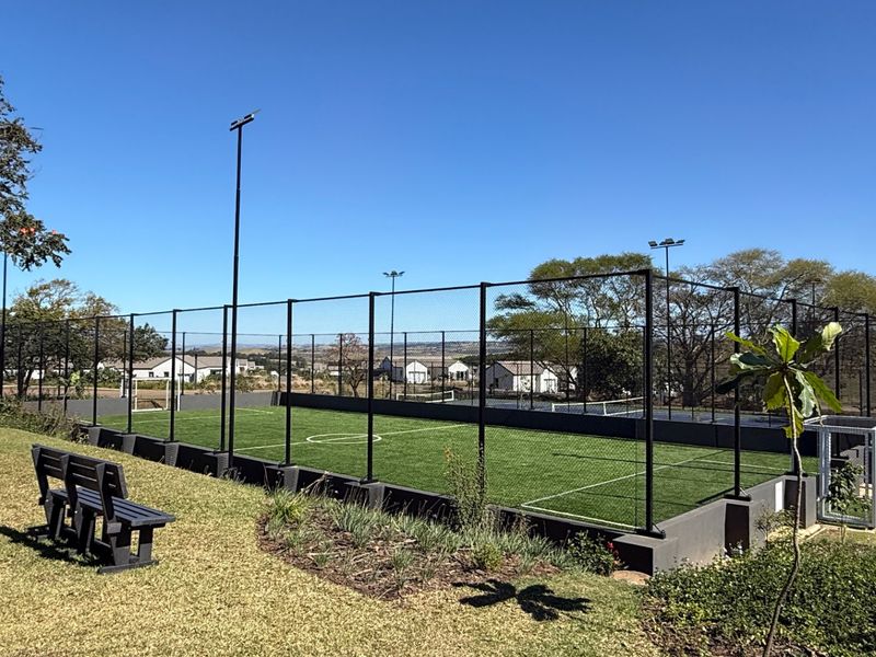 A well-maintained outdoor sports facility featuring artificial turf, perimeter fencing, and integrated floodlighting, set within a landscaped residential environment.