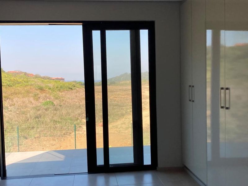 A bright, empty bedroom featuring modern built-in cupboards, tiled flooring, and a large sliding glass door opening to an outdoor area with scenic views.