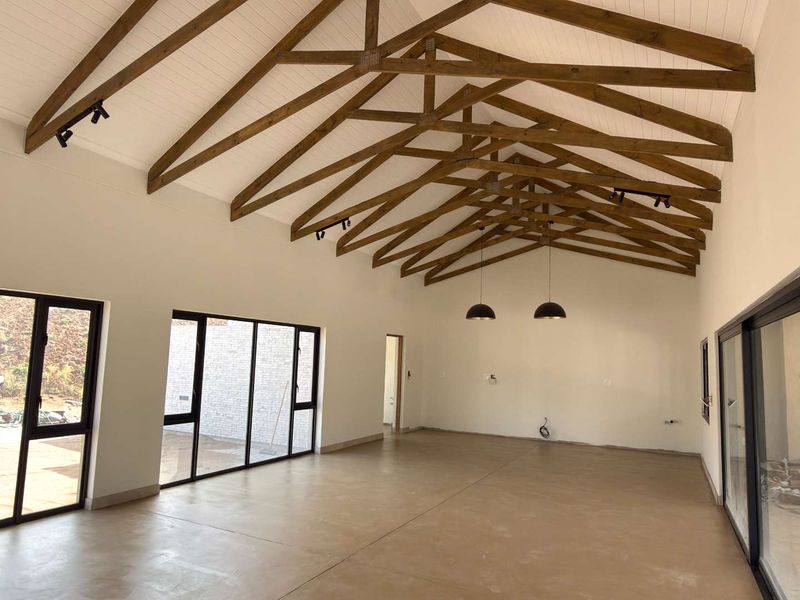 Spacious open-plan living area featuring high vaulted ceilings with exposed timber trusses, polished concrete floors, and large sliding doors providing abundant natural light.