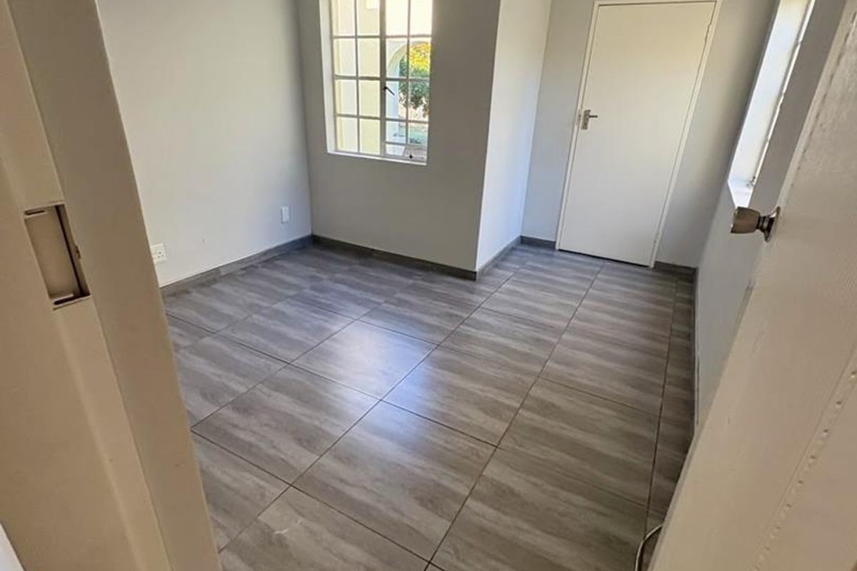 A clean, empty bedroom featuring modern wood-look floor tiles, a ceiling fan, and neutral wall finishes.
