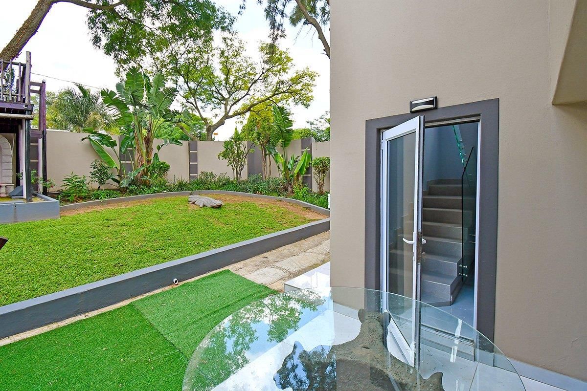 A private rear garden area featuring a manicured lawn, perimeter walling, and direct access to the interior via a glass-paneled door.