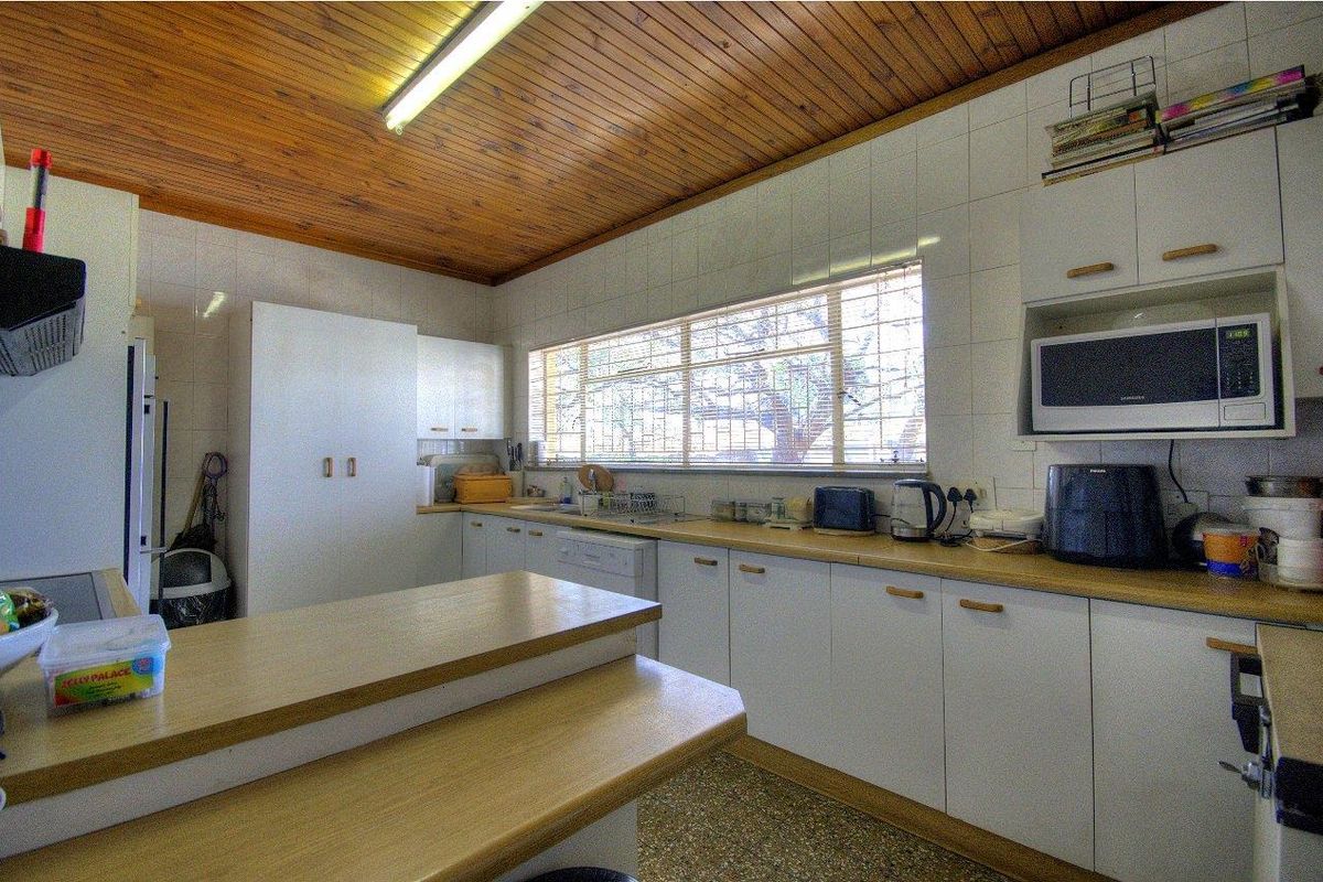 A functional kitchen featuring white cabinetry, laminate countertops, tiled splashbacks, and a distinctive timber-paneled ceiling with fluorescent lighting.