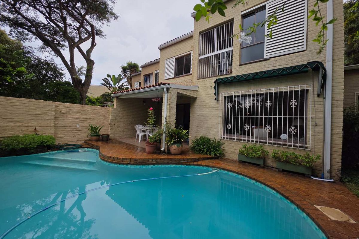 Rear view of a double-story cluster home featuring a swimming pool, covered patio area, and security bars on ground floor windows.