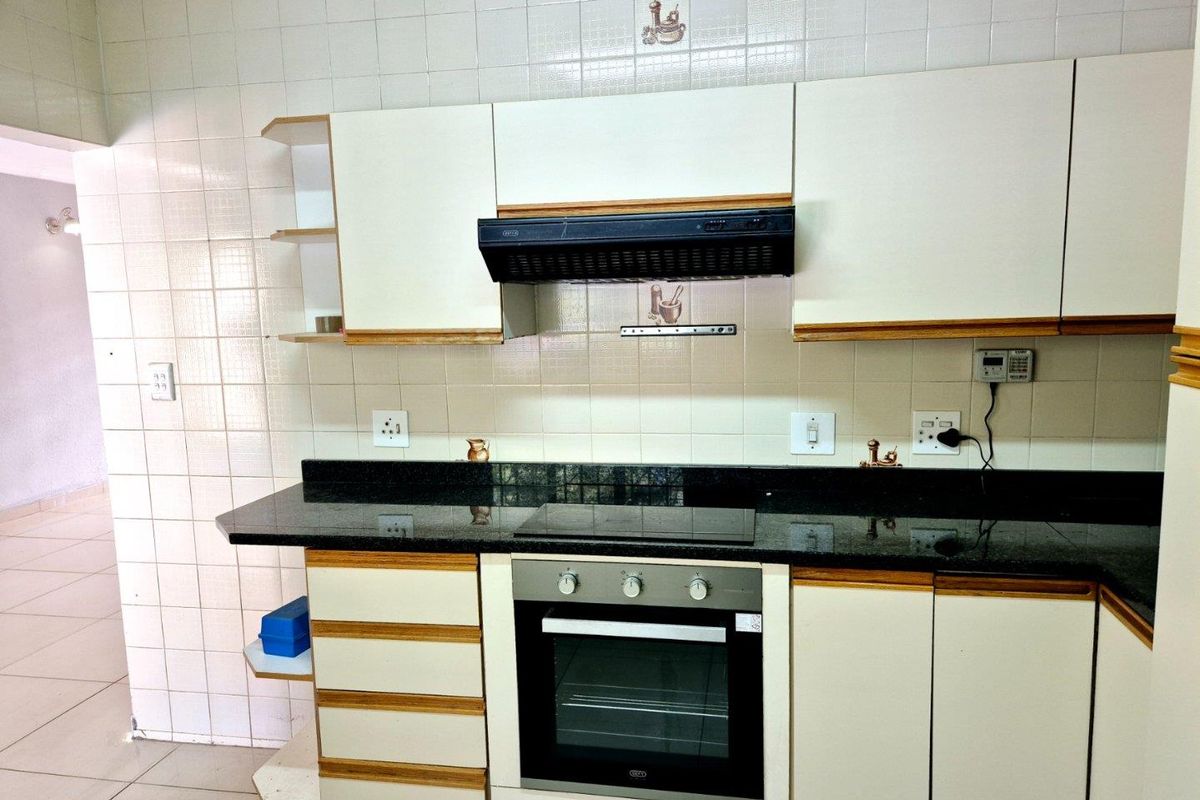 A functional kitchen featuring white cabinetry, granite countertops, a built-in oven, electric hob, and an extractor fan with tiled wall finishes.