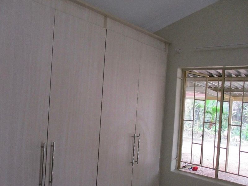 A bedroom featuring light-toned built-in cupboards and a window fitted with metal security bars.