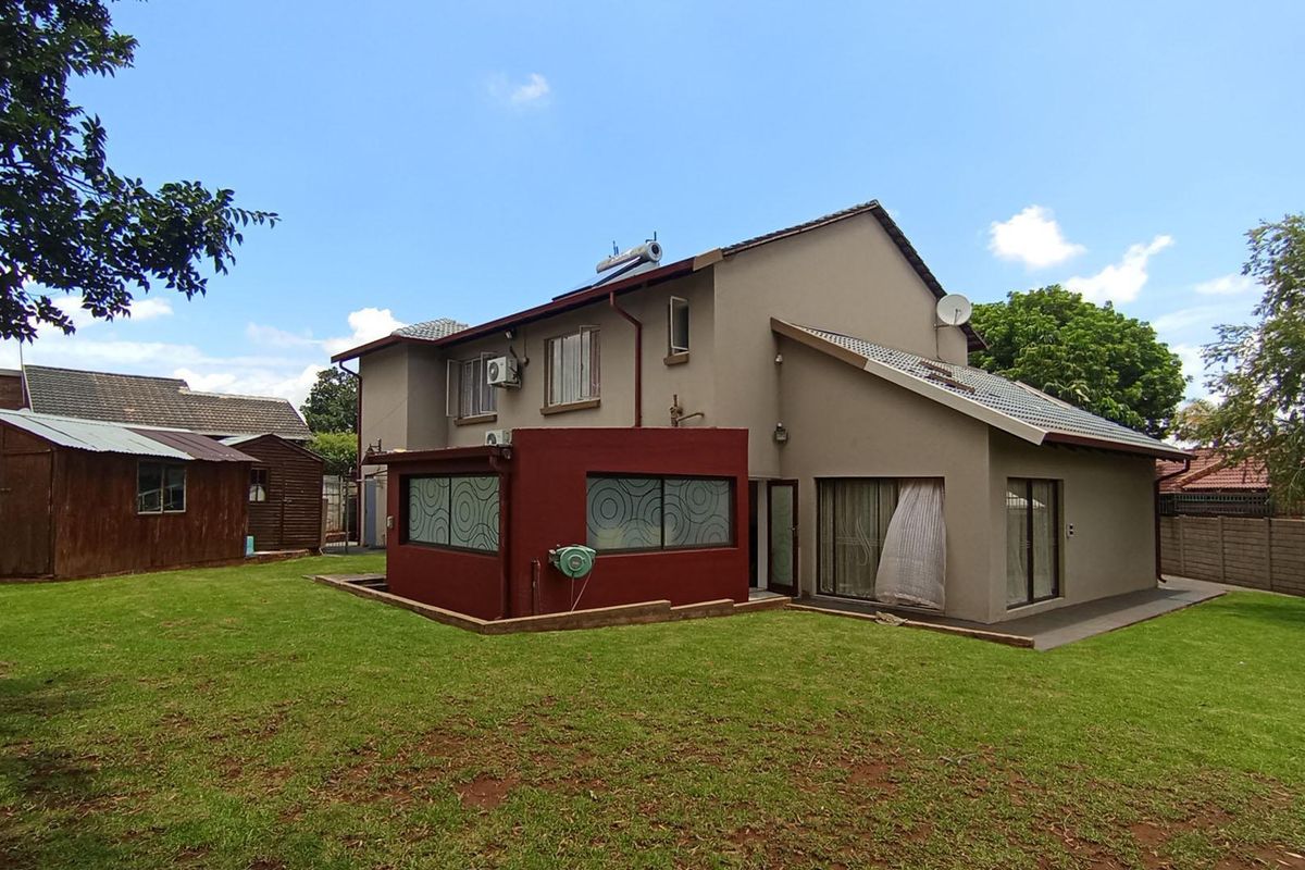 Rear view of the two-story house featuring a spacious lawn, a detached wooden shed, and a solar water heating system on the roof.