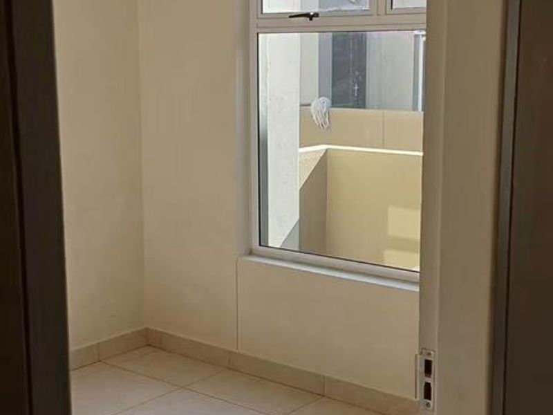 A bright, empty bedroom featuring neutral tiled flooring, a ceiling light fixture, and a window with a curtain track.