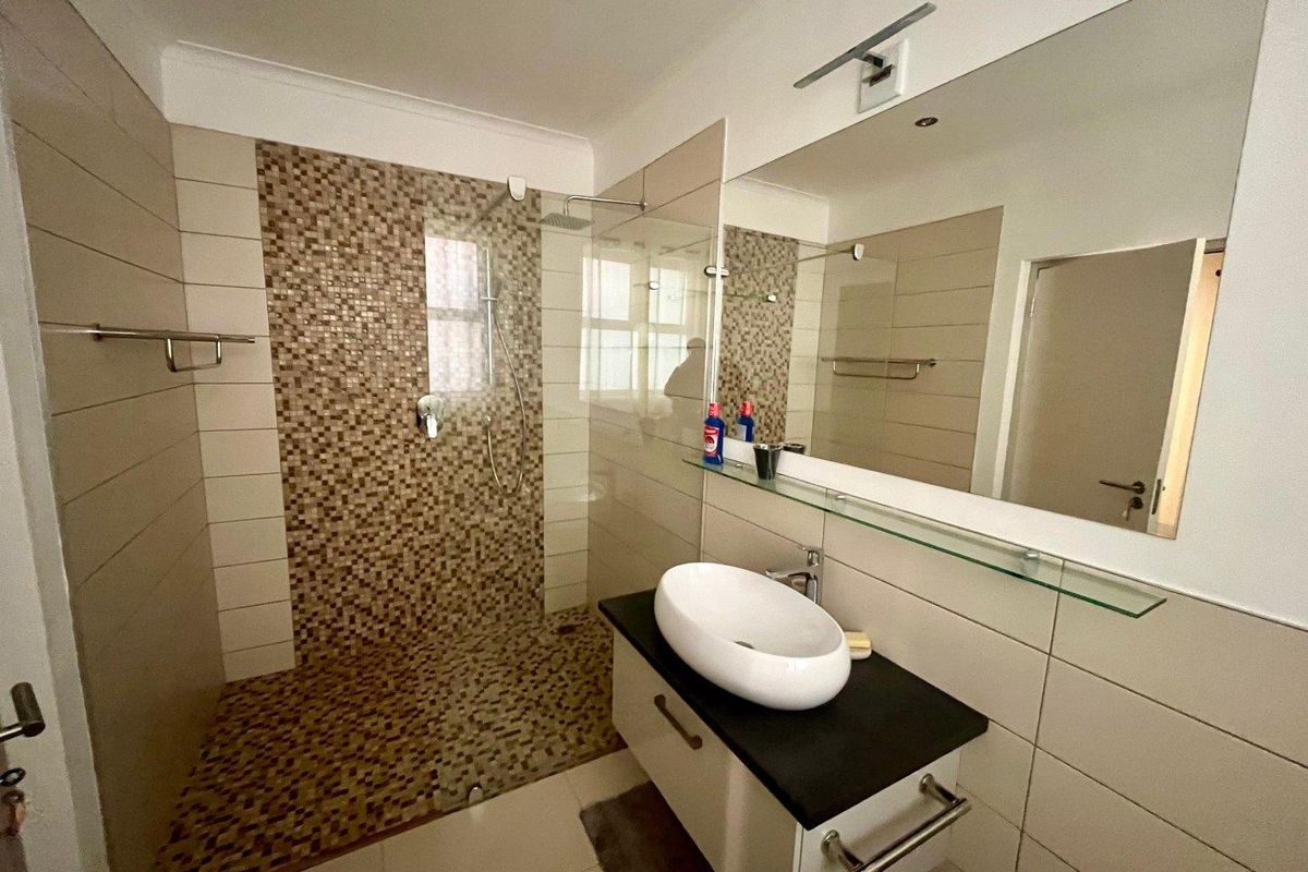 Modern bathroom featuring a walk-in shower with mosaic tile accents, a contemporary vessel sink on a vanity cabinet, and a large wall mirror.