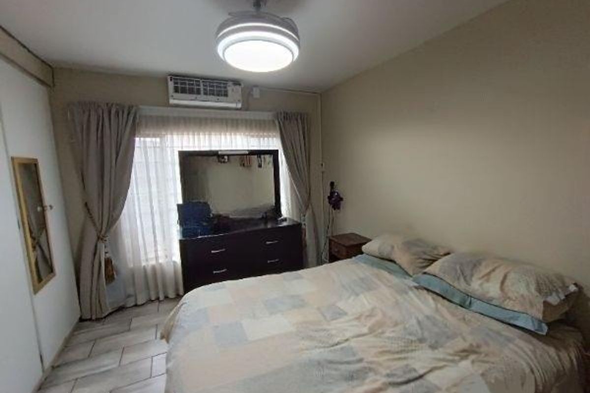 A bedroom featuring tiled flooring, a ceiling fan with integrated lighting, and a wall-mounted air conditioning unit.