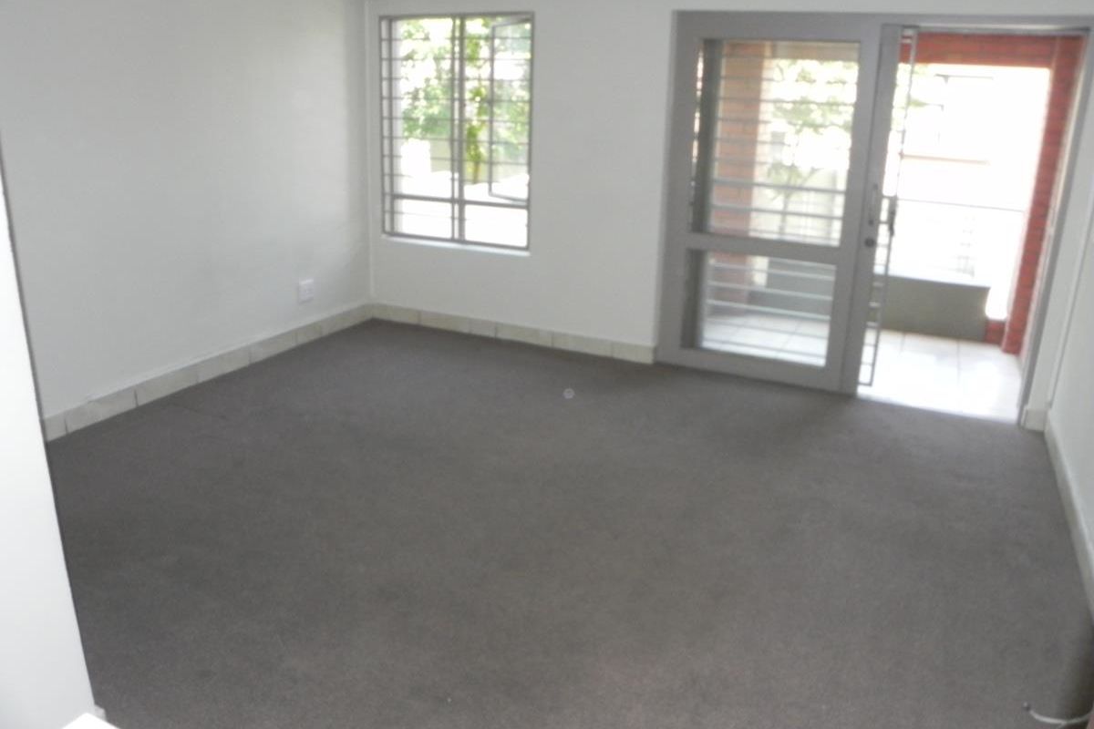 An empty living room featuring grey carpeting, security bars on the windows, and a sliding glass door providing access to an outdoor area.