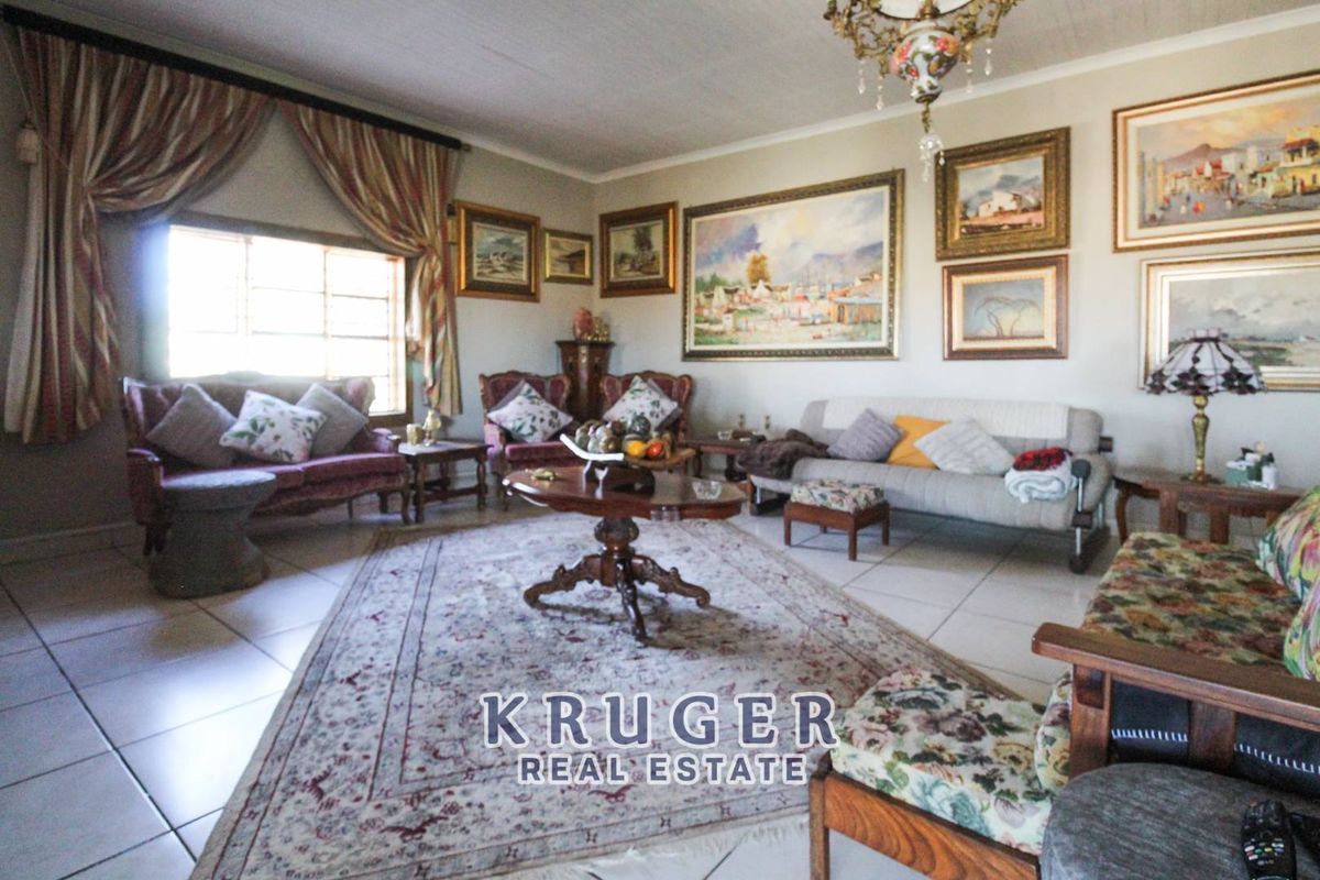 A spacious living room featuring tiled flooring, a decorative chandelier, and large windows, providing a comfortable and traditional lounge area.