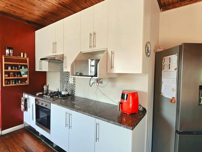 A kitchen featuring white cabinetry, granite countertops, built-in oven, gas hob, and extractor fan, set against a timber ceiling and wooden flooring.