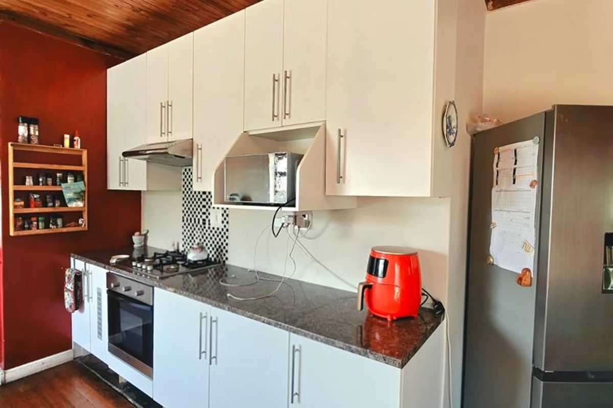 A kitchen featuring white cabinetry, granite countertops, built-in oven, gas hob, and extractor fan, set against a timber ceiling and wooden flooring.