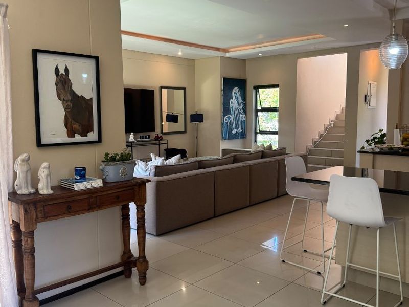 Spacious open-plan living area featuring polished porcelain tiles, recessed ceiling lighting, a modern staircase, and a functional kitchen island with breakfast bar seating.