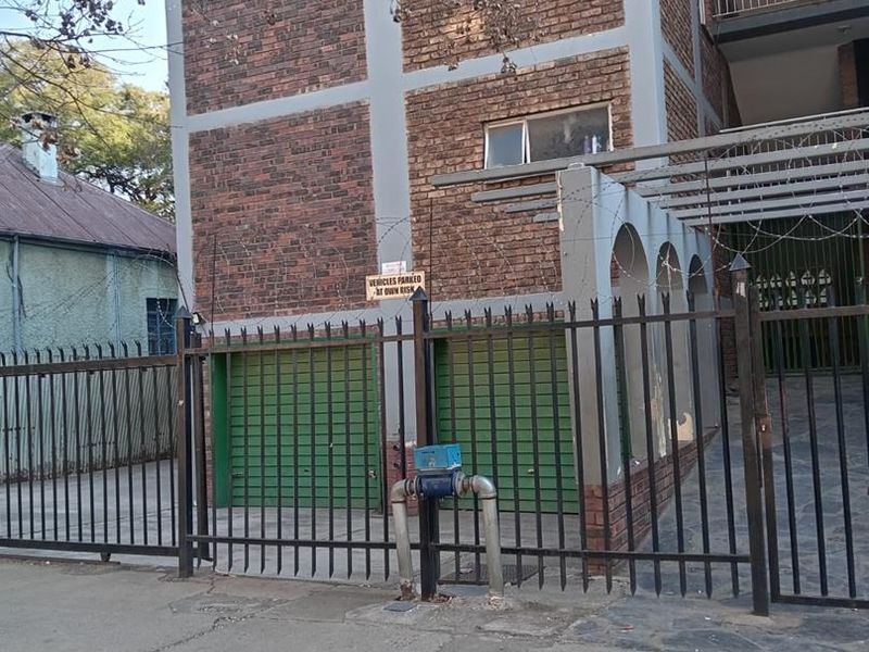 Street view of an apartment building featuring a brick facade, metal security fencing, and ground-level garage access.