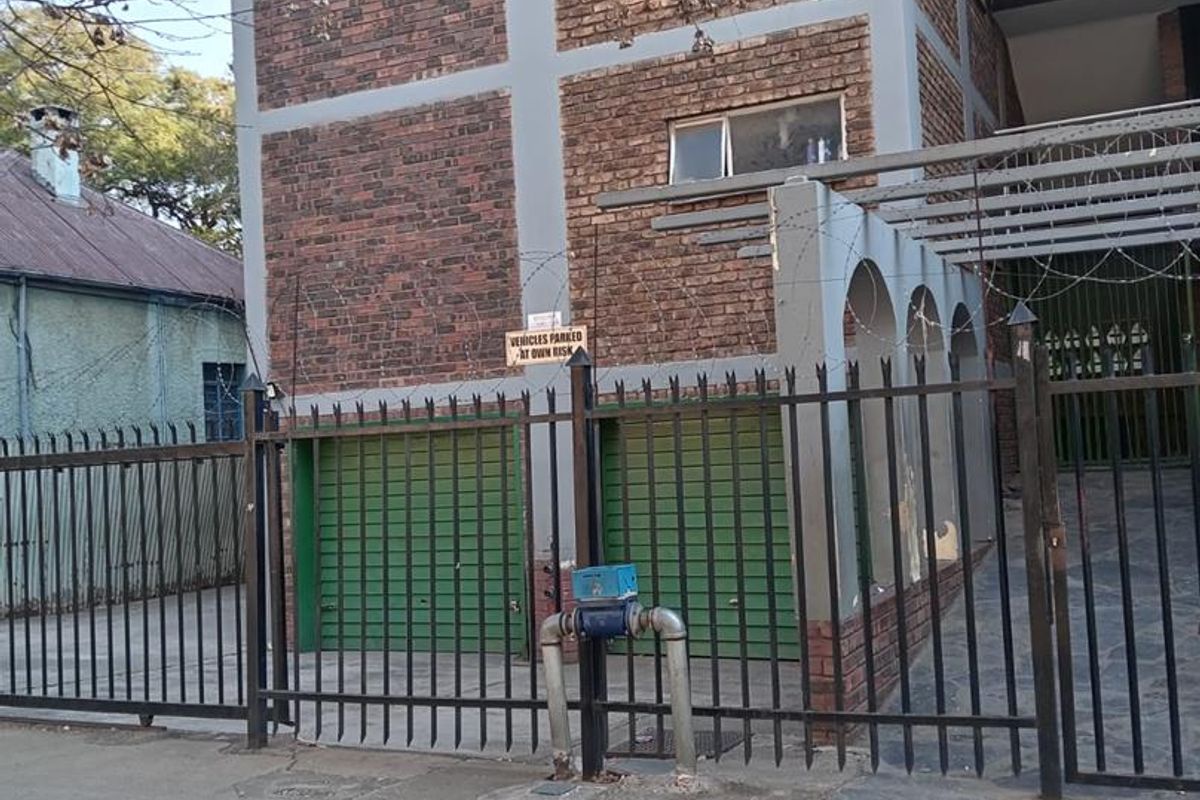 Street view of an apartment building featuring a brick facade, metal security fencing, and ground-level garage access.