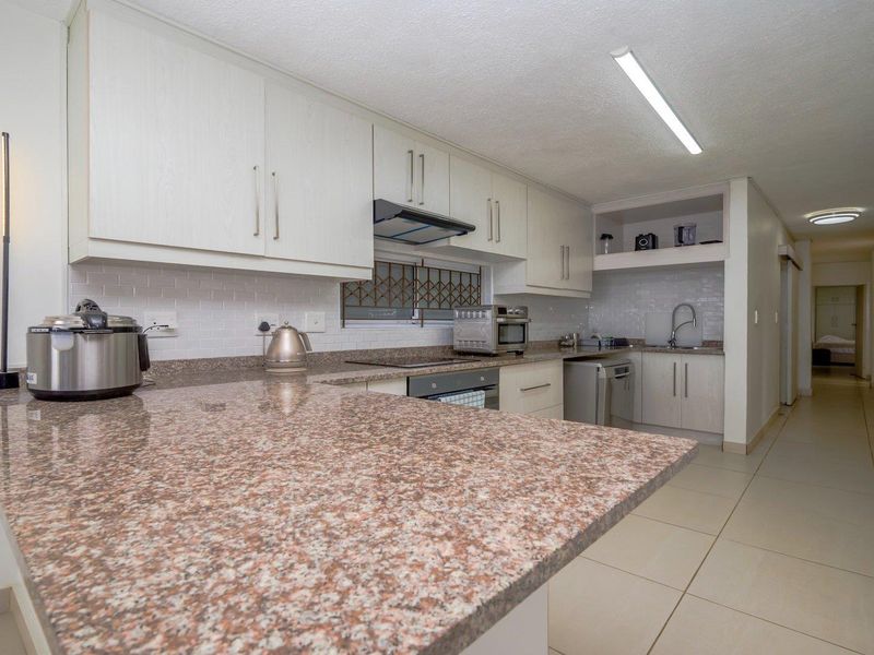 A functional kitchen featuring granite countertops, subway tile backsplash, built-in cabinetry, and integrated appliances, leading into a tiled hallway.