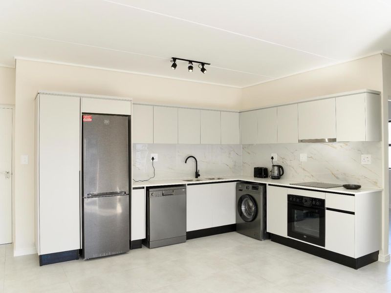 Modern kitchen featuring sleek white cabinetry, marble-look splashback, integrated oven, electric cooktop, and high-quality finishes throughout.