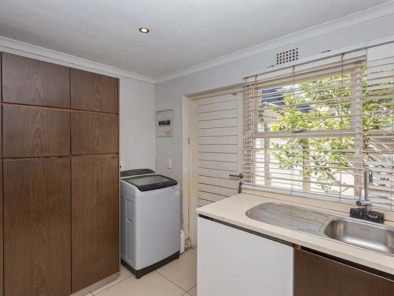 Functional laundry room featuring built-in storage cabinetry, a stainless steel sink with mixer tap, and tiled flooring with natural light from the window.