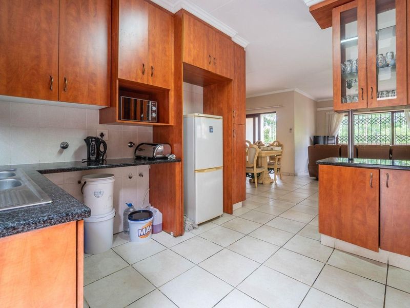 Open-plan kitchen featuring wooden cabinetry, granite countertops, and tiled flooring, flowing into the adjacent dining and living area.