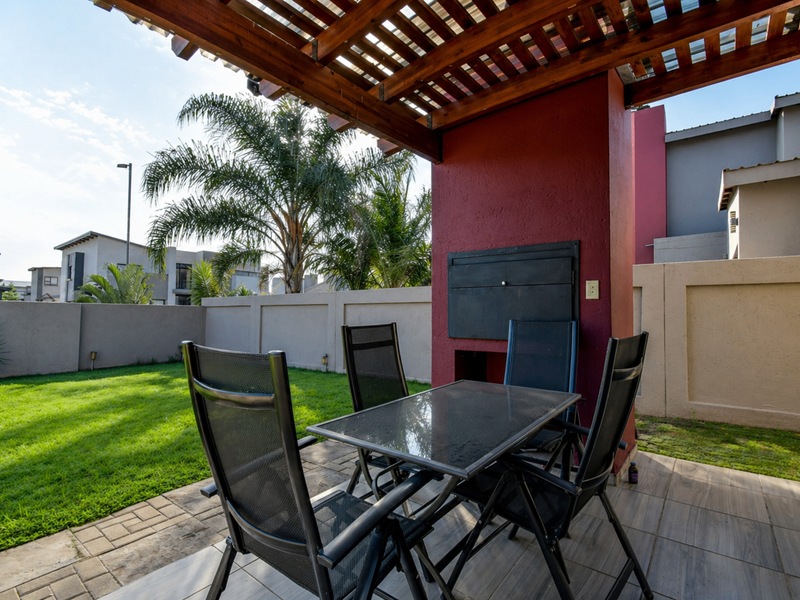 Covered patio area featuring a timber pergola and a built-in braai, overlooking a private garden with paved and lawn sections.