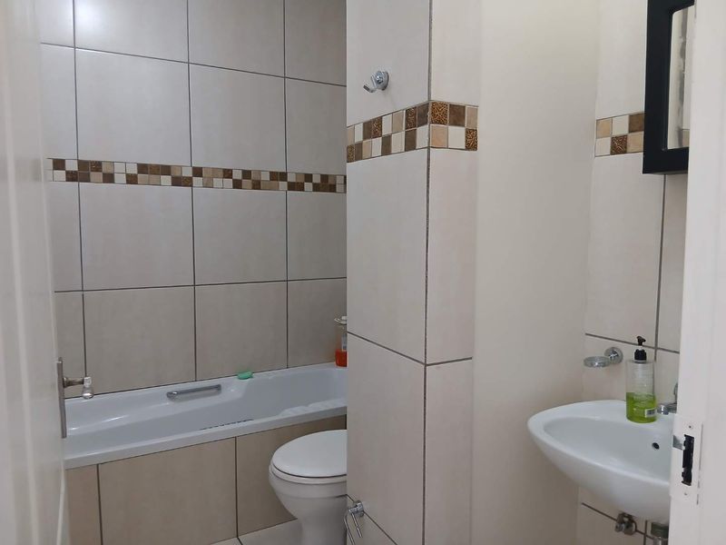 A functional bathroom featuring a bathtub, toilet, and wall-mounted basin with neutral tiled walls and a decorative mosaic border.