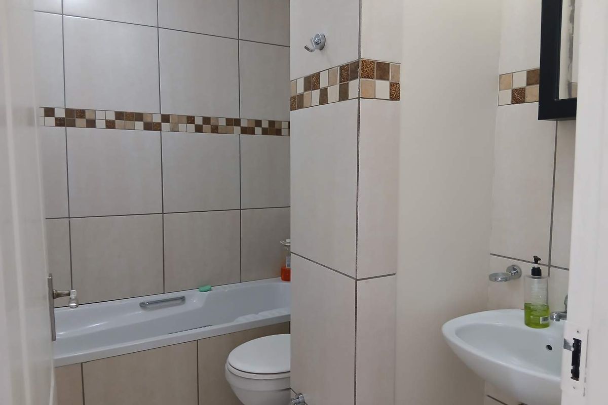 A functional bathroom featuring a bathtub, toilet, and wall-mounted basin with neutral tiled walls and a decorative mosaic border.