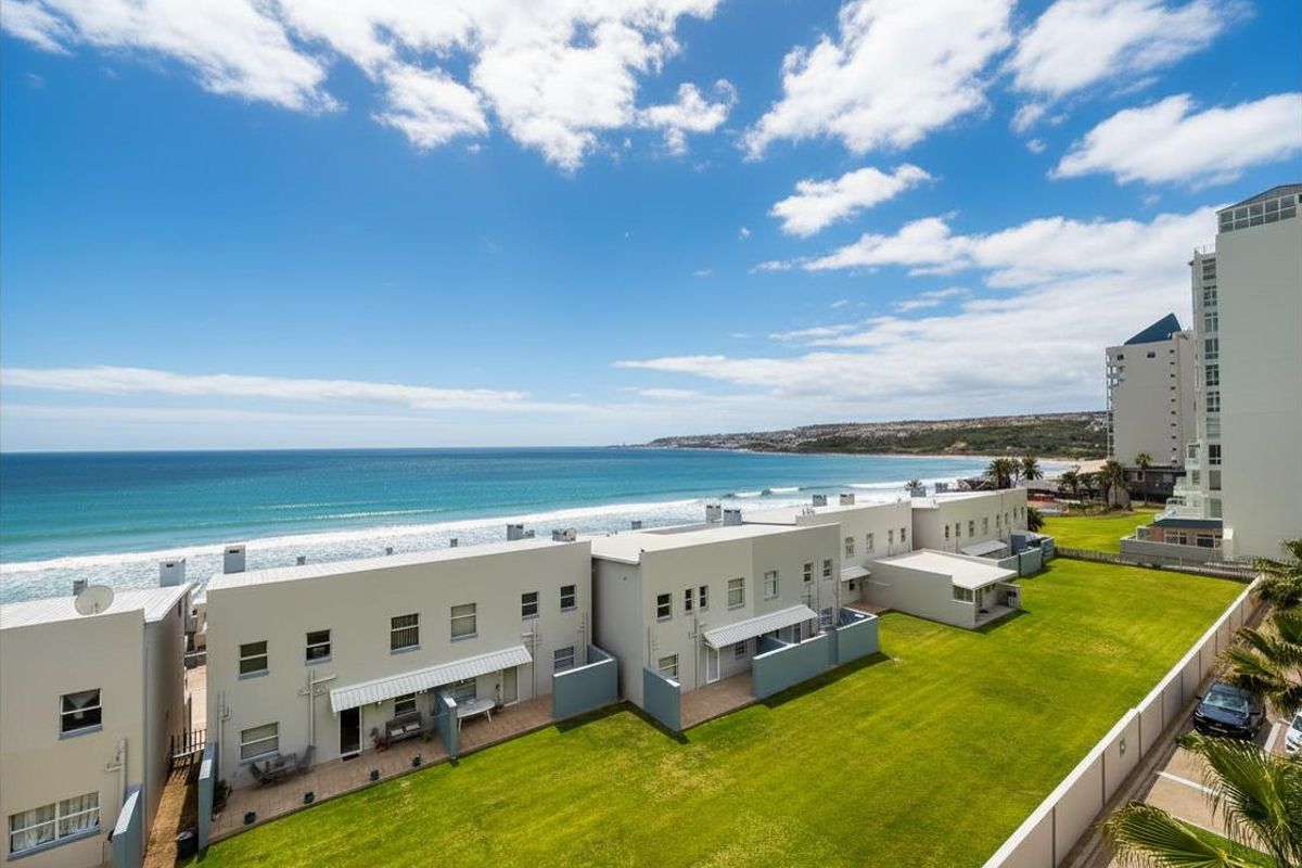 An elevated aerial view of the apartment complex, showcasing the manicured lawn, rear patio areas, and direct proximity to the coastline and beach.