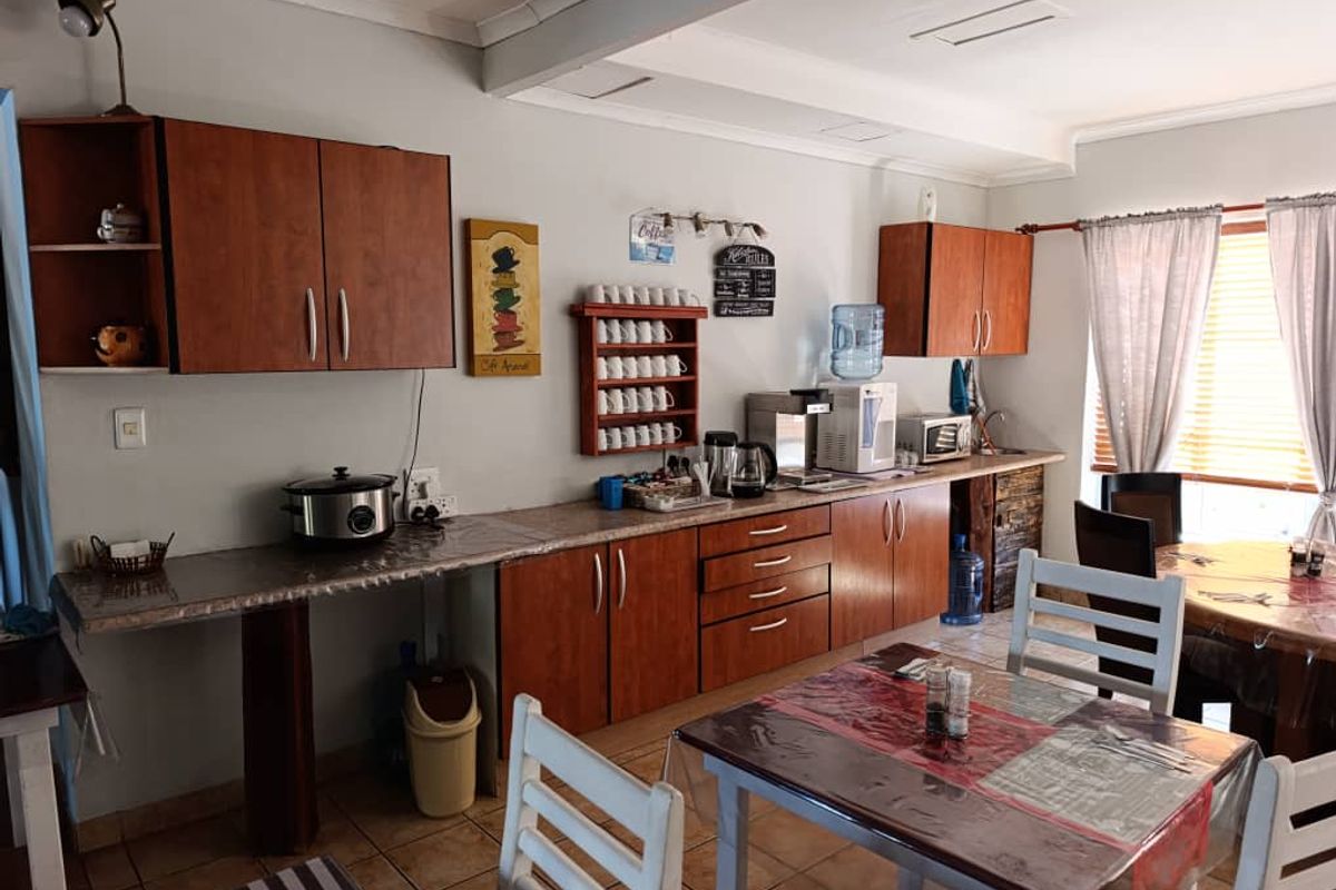 A functional kitchen area featuring wood-finish cabinetry, laminate countertops, and tiled flooring, suitable for commercial or office breakroom use.