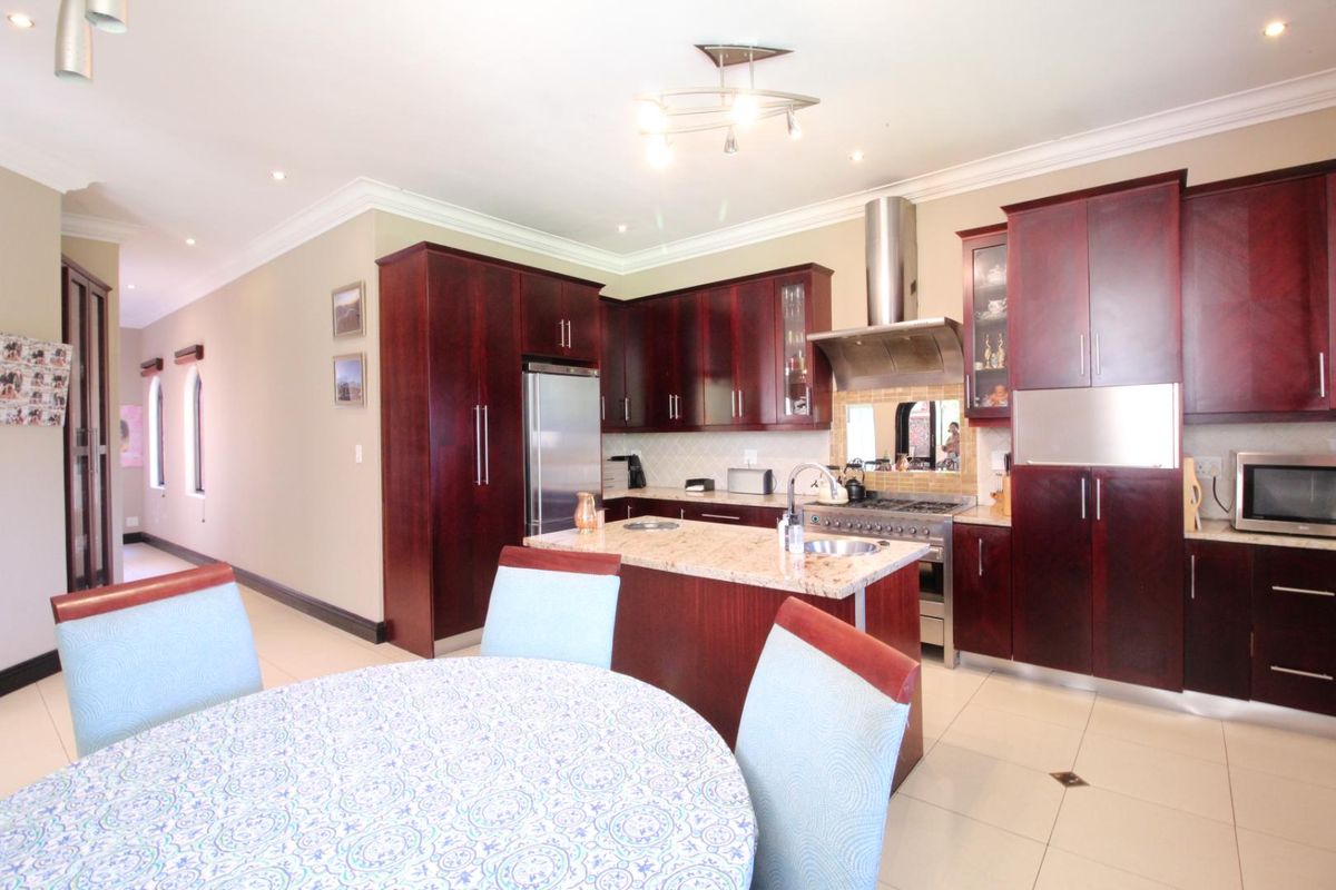 A spacious kitchen featuring dark wood cabinetry, granite countertops, a central island with a prep sink, and a stainless steel gas range with extractor.
