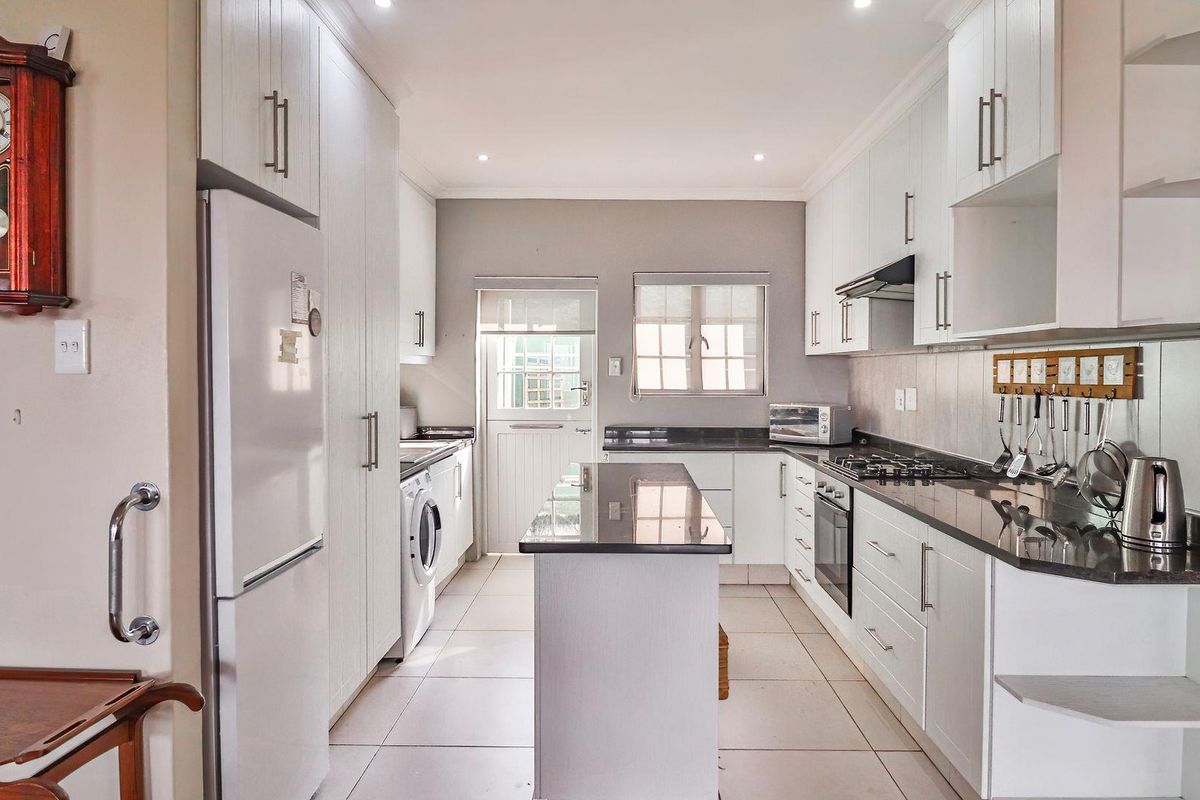 Modern galley-style kitchen featuring white cabinetry, dark granite countertops, a central island, built-in oven, gas hob, and integrated laundry appliance space.