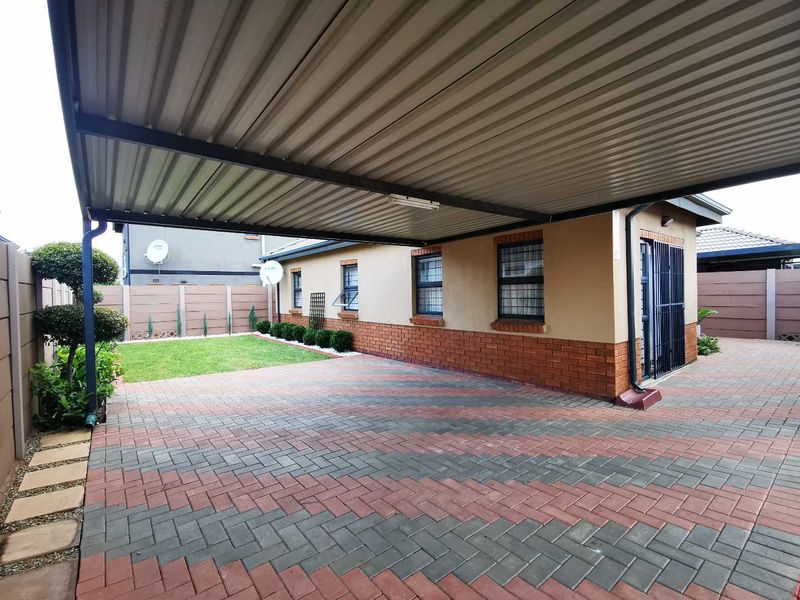 A well-maintained rear exterior featuring a spacious paved carport, brick facade, and a neat garden area enclosed by a precast concrete wall.