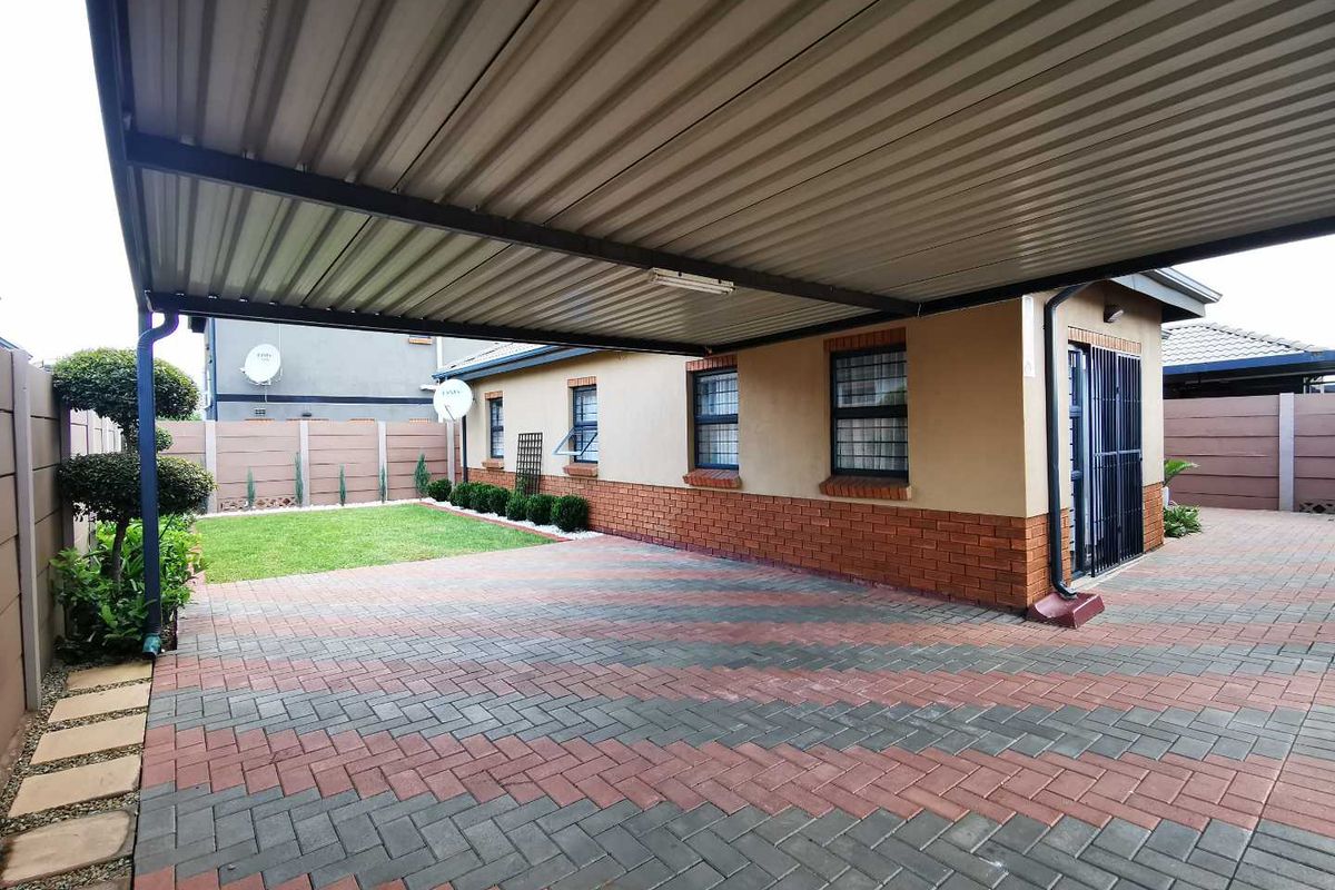 A well-maintained rear exterior featuring a spacious paved carport, brick facade, and a neat garden area enclosed by a precast concrete wall.