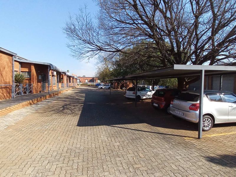 Exterior view of an industrial property featuring a paved driveway, covered parking bays, and brick-faced building facades.