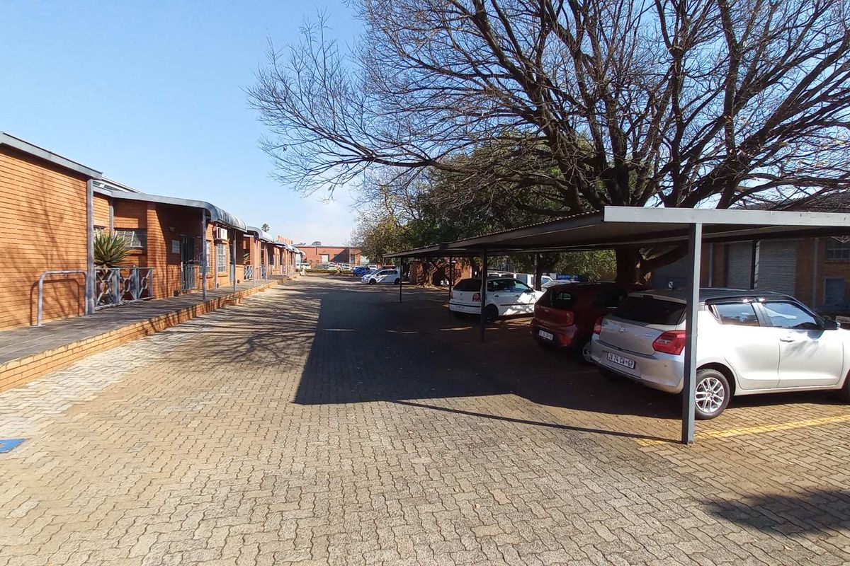 Exterior view of an industrial property featuring a paved driveway, covered parking bays, and brick-faced building facades.