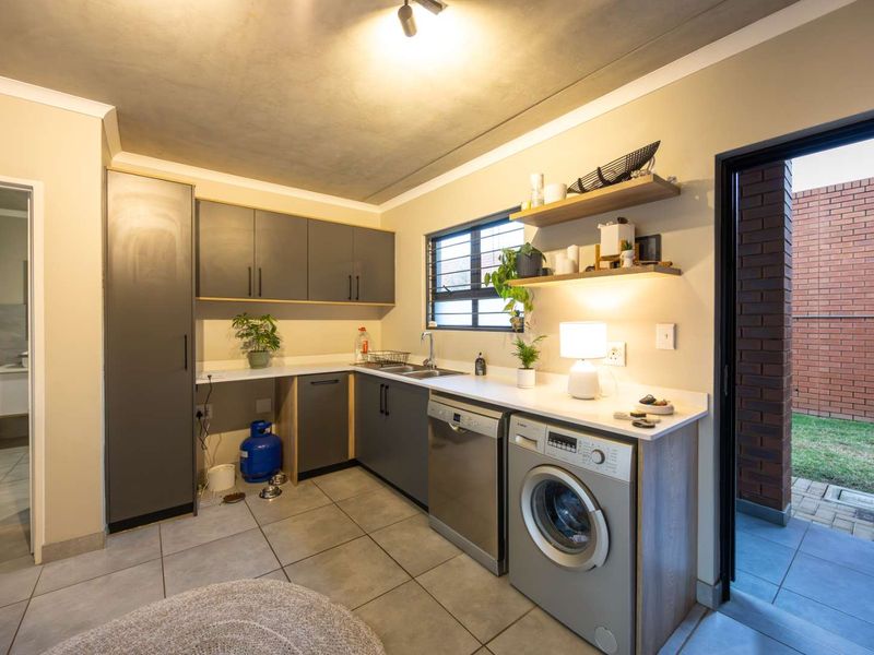 A functional scullery featuring modern grey cabinetry, a double sink, tiled flooring, and direct access to an outdoor area.