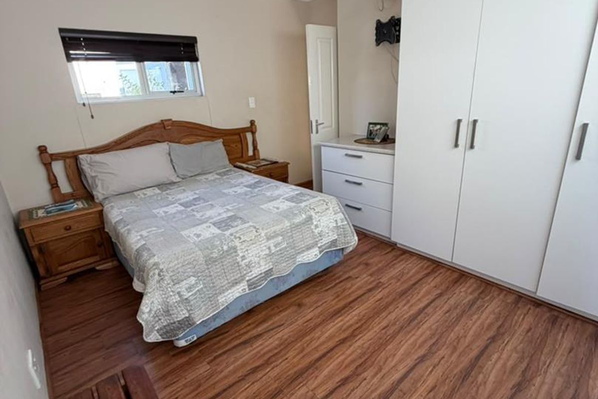 A functional bedroom featuring laminate flooring, built-in white cupboards, and a window with a fitted blind.